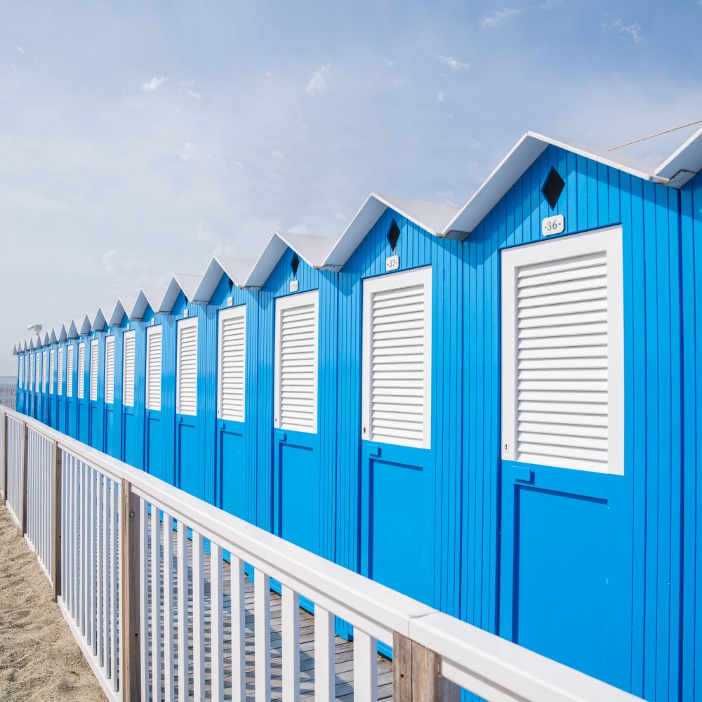 Traditional Italian beach huts on a bright sunny day,Blue beach cabins arranged in rows up on the seashore,Varazze Liguria Italy.