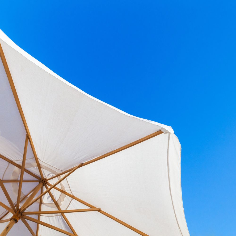 White outdoor umbrella under bright blue sky in summer day, resort background photo
